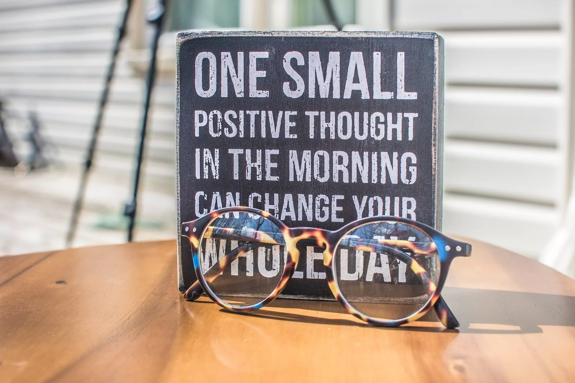 A motivational quote on a sign with eyeglasses in front, sitting on a wooden table outdoors.